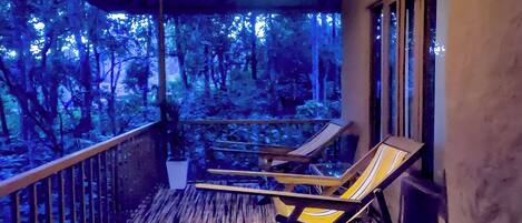 A balcony with wooden flooring and two lounge chairs facing a forested area.