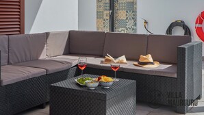 A modern outdoor seating area with a grey woven sofa, a small table with snacks and drinks, and a patterned wall in the background. - Villa Mauruuru 10 Minutes Walking From Marina Rubicón, Heated Pool&bbq (CN)