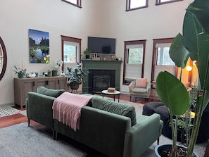 Un salon avec un canapé vert, une cheminée, un téléviseur et diverses plantes.