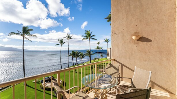 Ein Balkon mit Glastisch und Stühlen, mit Blick auf einen Strand mit Palmen und den Ozean.