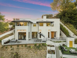 A modern two-story house with a flat roof, large windows, and a balcony.