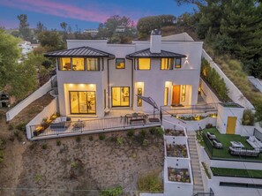 A modern two-story house with multiple balconies, large windows, and a well-maintained garden.