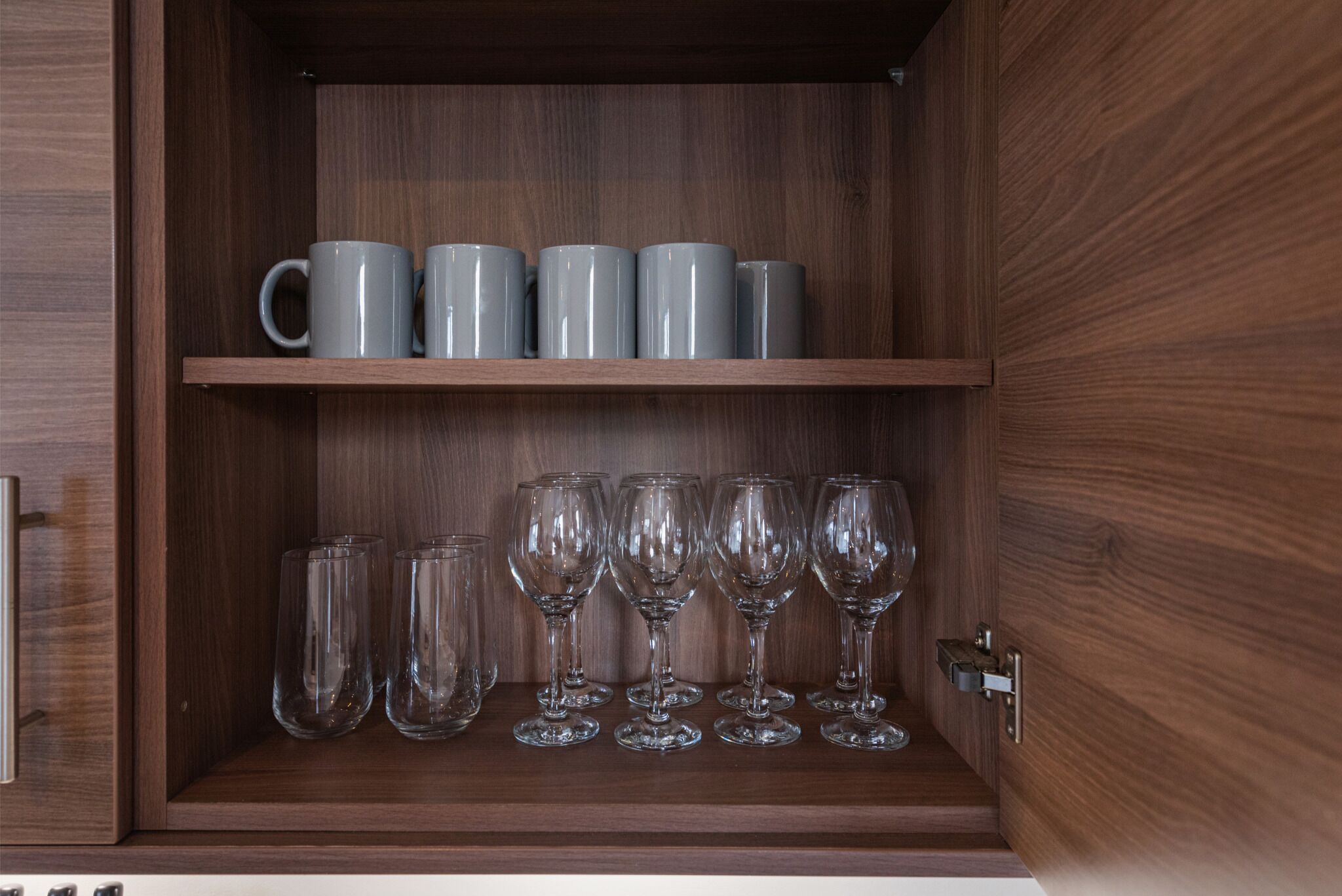 Ein Holzschrank mit zwei Einlegeböcken; die obere Ablage zeigt sechs graue Tassen, und die untere Ablage enthält sechs klare Weingläser.