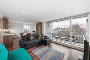 A modern living room with a grey sectional sofa, a teal armchair, and a large window offering a city view.