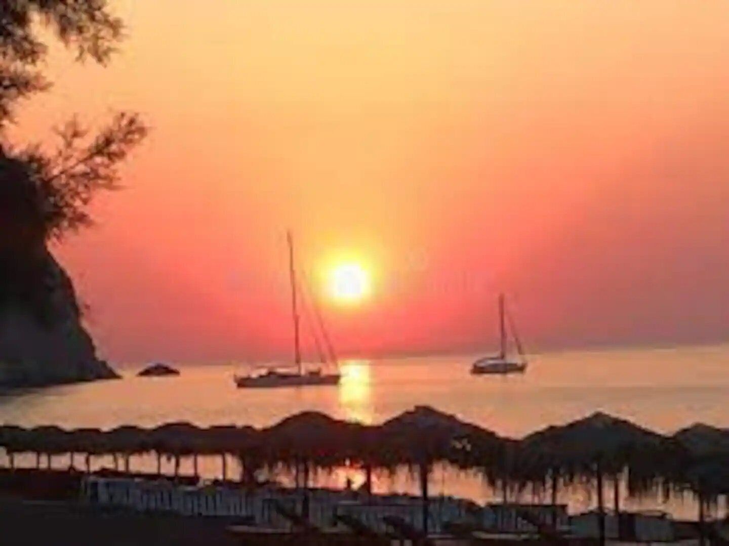Ein Sonnenuntergang über einem ruhigen Meer mit Booten und einem Hafen.
