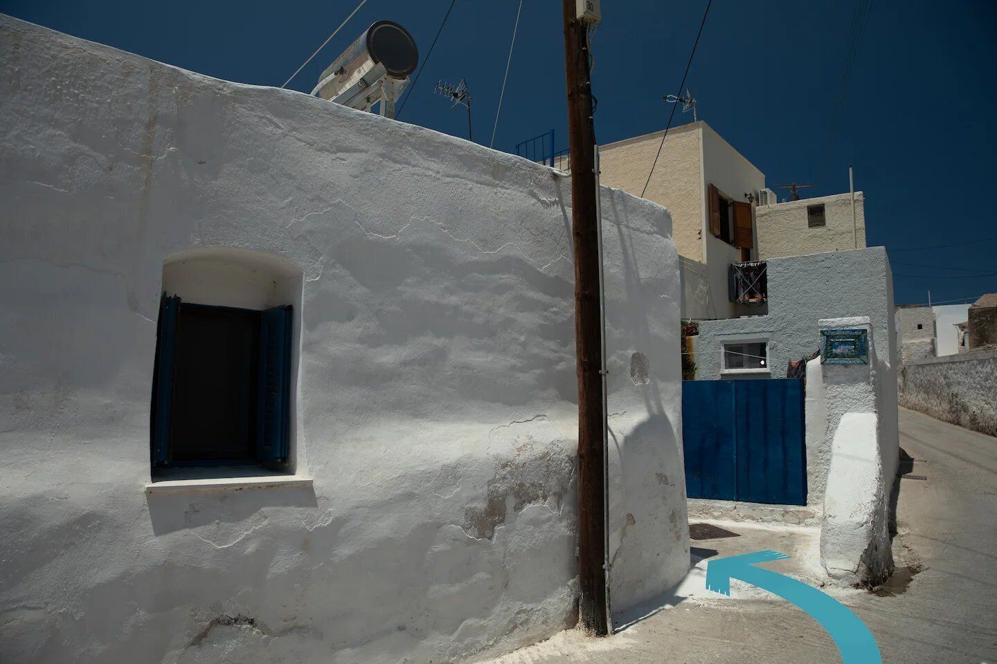 A narrow street with white buildings, a blue gate, and a satellite dish on one of the buildings.