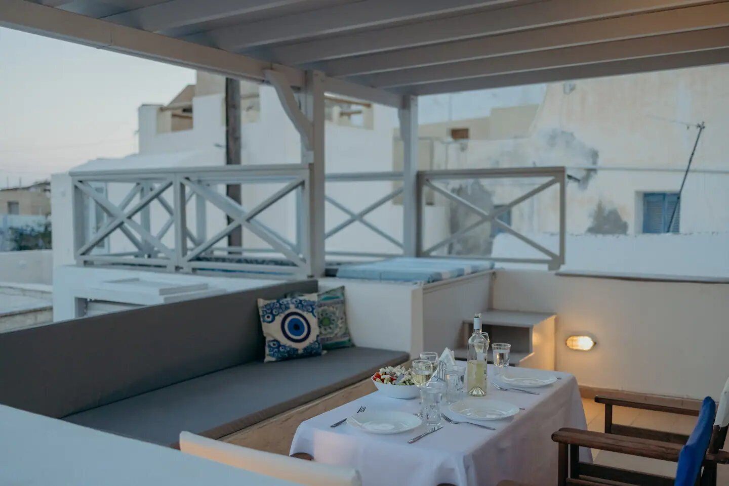 A rooftop terrace with a dining table set for two, a cushioned seating area, and a view of the cityscape.