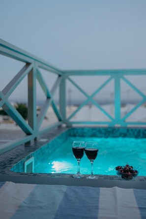 Escena junto a la piscina, con dos copas de vino tinto y un bol de cerezas sobre una mesa.