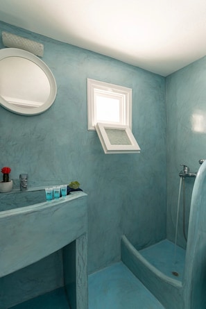 A bathroom with a blue marble wall, a white sink with toiletries, a framed mirror, and a shower area. - Panoramic Argyro's IO House with Jacuzzi (Santorini)