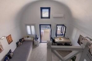 A compact room with a high ceiling, a small window, a dining area with a table and chairs, and a white air conditioning unit mounted on the wall. - Panoramic Argyro's IO House with Jacuzzi (Santorini)