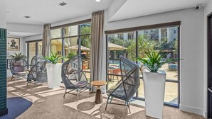 Habitación de hotel moderna con ventanas amplias, sillas de mimbre, una mesita redonda y plantas en macetas.
