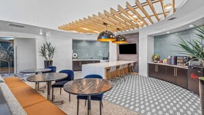 Una cocina moderna con barra, una zona de estar con mesas redondas y un suelo con diseño.