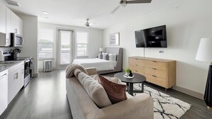 A modern hotel room with a kitchenette, a bed, a sofa, a TV, and a wooden cabinet. - Landing | Amazing Studio, Pool, Gym (Dallas)