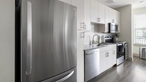 A modern kitchen with stainless steel appliances, white cabinetry, and a granite countertop. - Landing | Amazing Studio, Pool, Gym (Dallas)