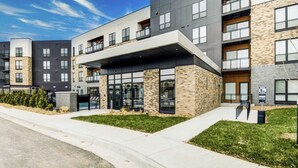 A modern multi-story building with a covered entrance, large windows, and a mix of stone and concrete exterior. - Landing | Stunning 1BD, Yoga Studio, Courtyard (Kansas City)