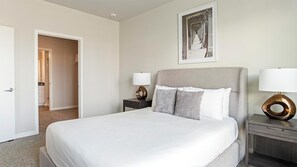 A hotel room with a large bed, two bedside tables, a wall-mounted picture, and a door leading to a bathroom.