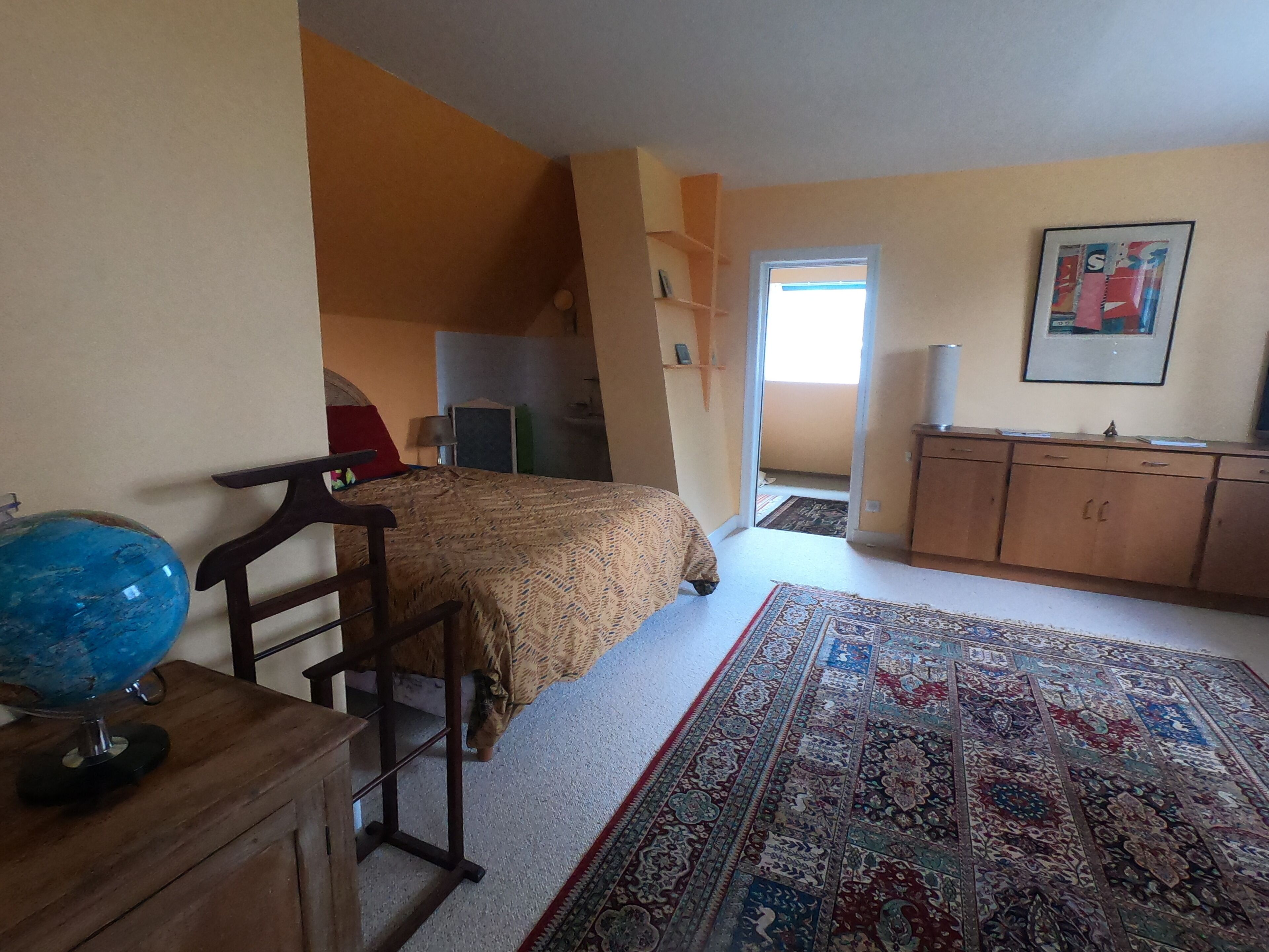 A bedroom with a bed, a desk, a globe, a patterned rug, and a wardrobe.