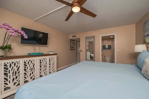 A bedroom with a bed, a ceiling fan, a TV, and a dresser with decorative panels. - Pelican Inlet D229- The Chubby Mermaid (St. Augustine)