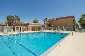A swimming pool with a wooden deck, lounge chairs, and a building with a red roof. - Pelican Inlet D229- The Chubby Mermaid (St. Augustine)