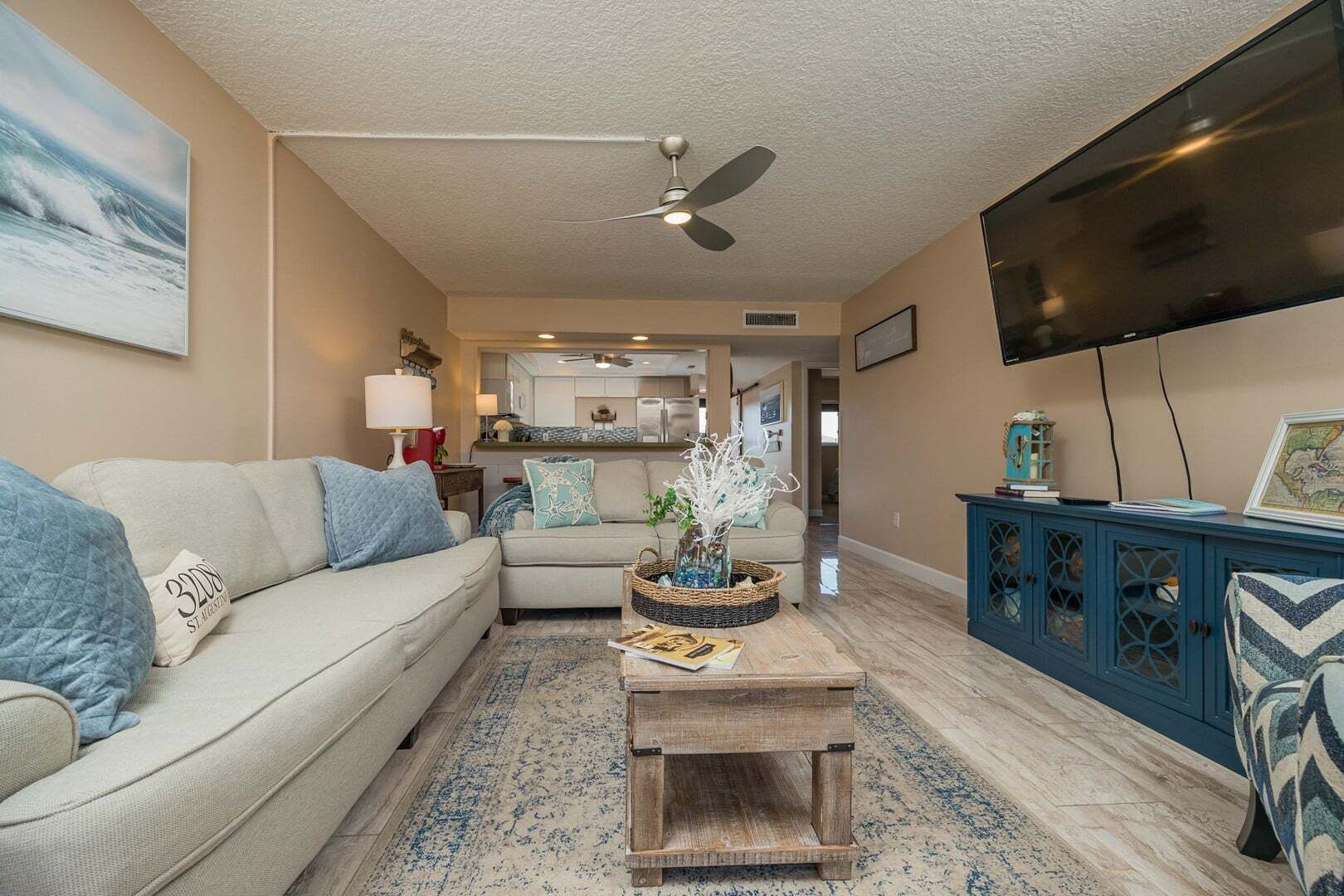 A living room with a sofa, coffee table, TV, and a view into the kitchen.