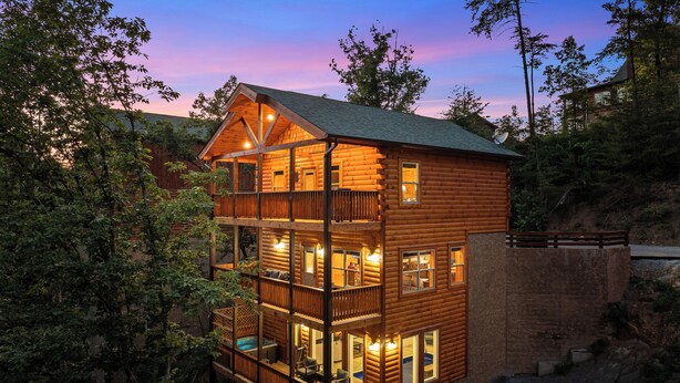 Eine mehrstöckige Blockhütte mit Balkon und Terrasse, umgeben von Bäumen.