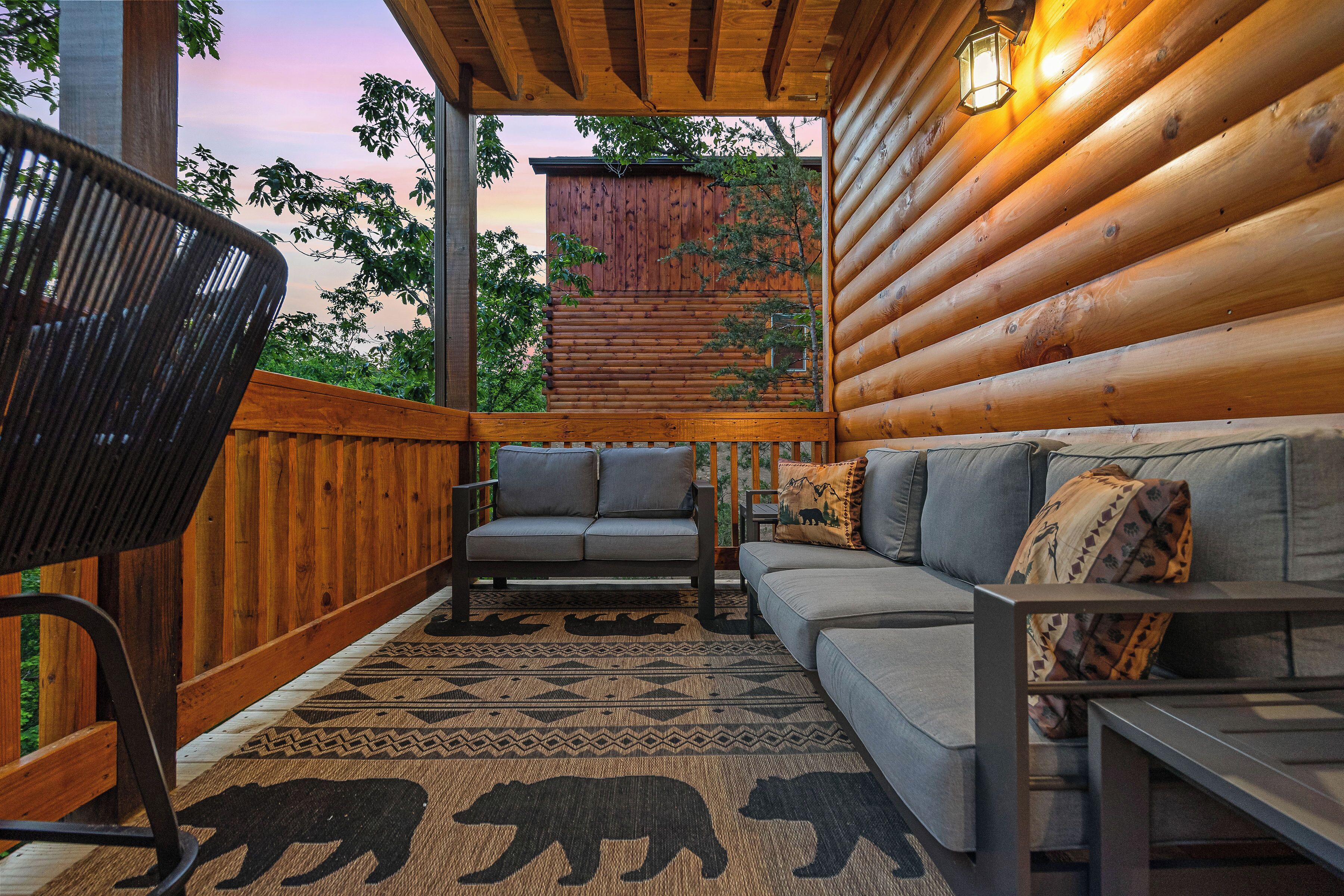 Une cabane en rondins avec une terrasse en bois, un canapé, un fauteuil et un tapis à motifs.