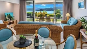 Un salon moderne avec une grande table en verre, des meubles en osier et une vue imprenable sur un lac et des montagnes.