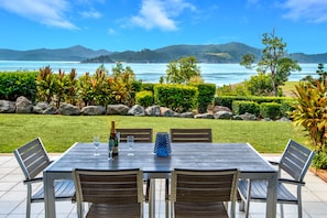 An outdoor dining area with a view of the sea and hills. - Frangipani Lodge F5, Frangipani F5 on Hamilton Island (Hamilton Island)