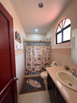 A bathroom with a shower curtain featuring a surf theme, a toilet, a sink, and a mirror. - Jaco Hideaway: 1 minute walk to direct beach access.
Gated community with pool. (Jacó)