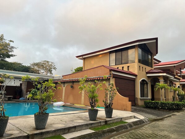 A modern house with a pool, potted plants, and a clear sky. - Jaco Hideaway: 1 minute walk to direct beach access.
Gated community with pool. (Jacó)