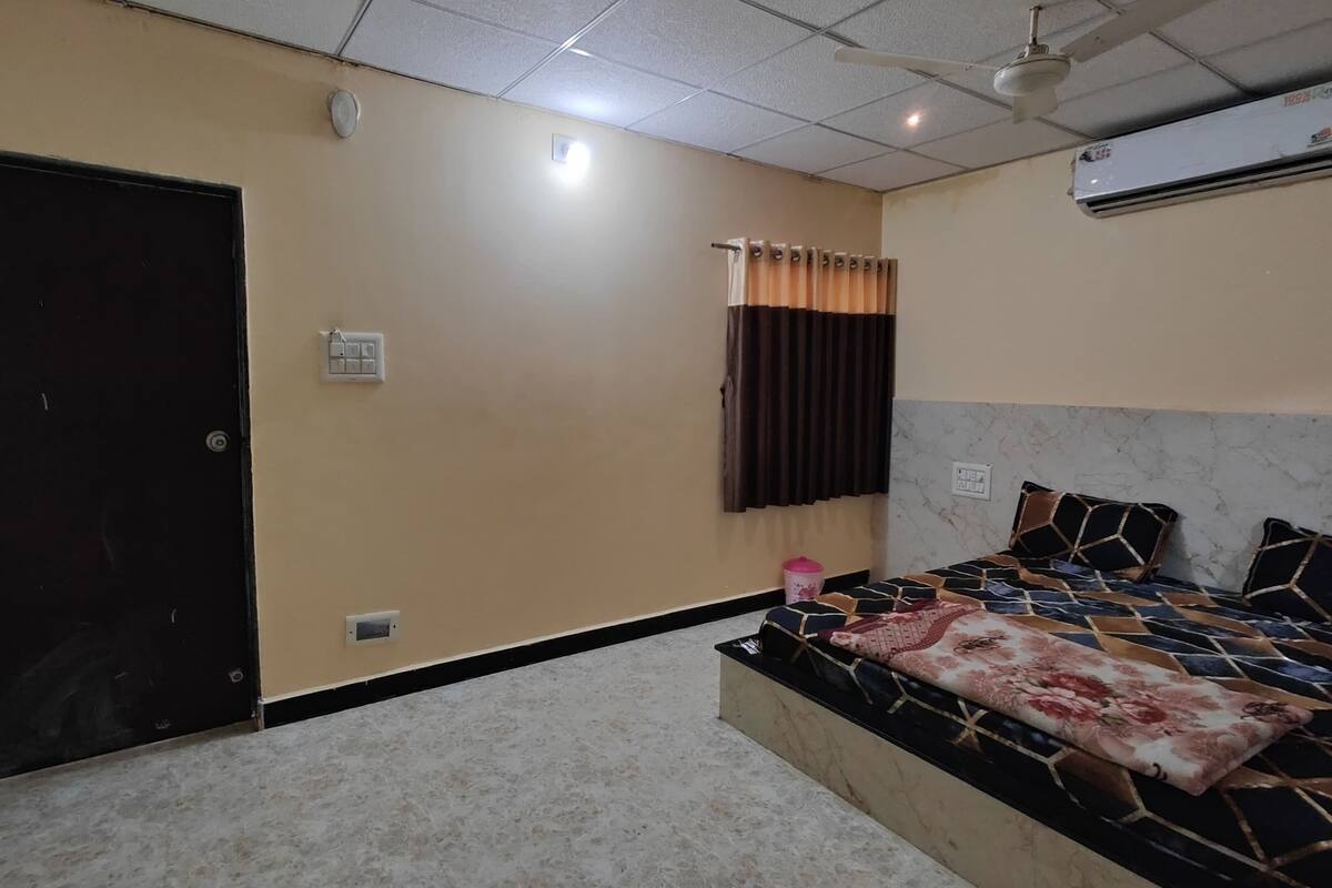 A bedroom with a bed, a door, an air conditioning unit, and a window with curtains.