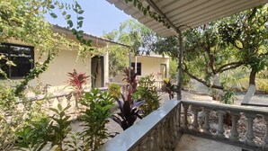 A covered outdoor area with a stone balustrade, various potted plants, and a building with a beige facade and a window with a black frame. - Gir Forever  (Talala)