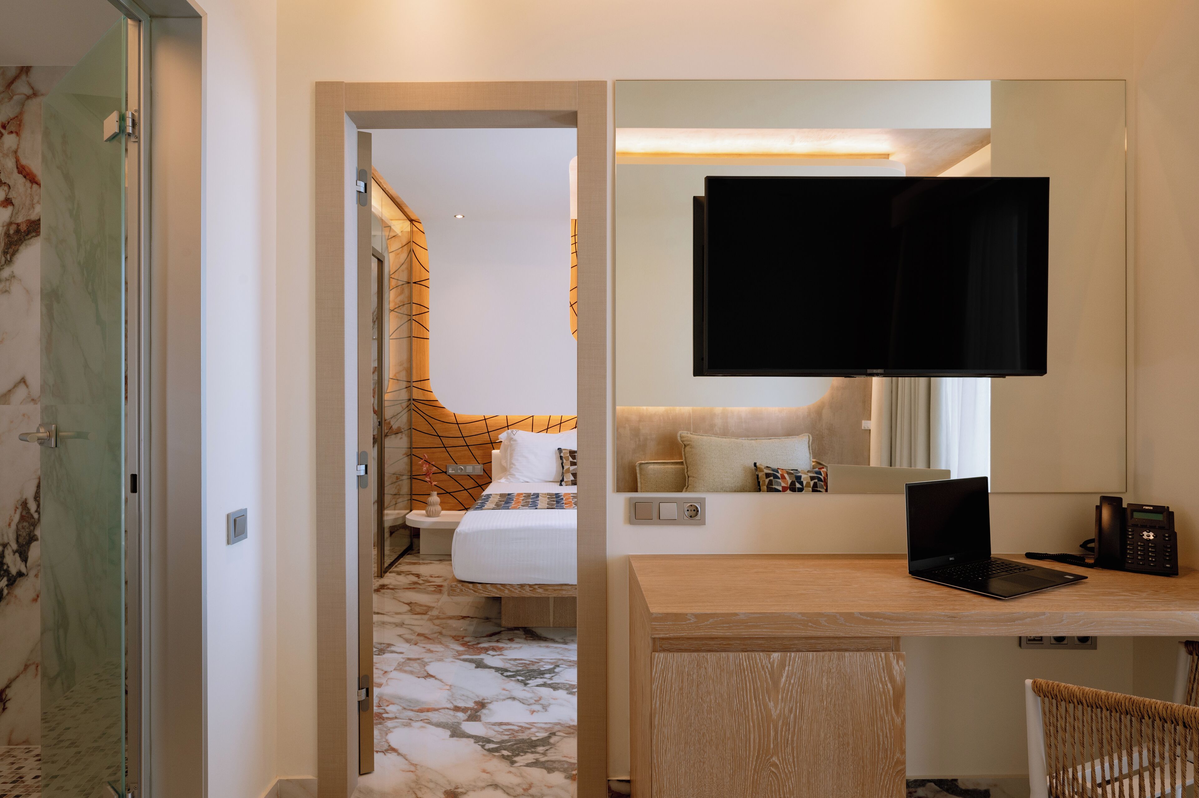 A hotel room with a bed, a desk with a laptop, a television, and a telephone.