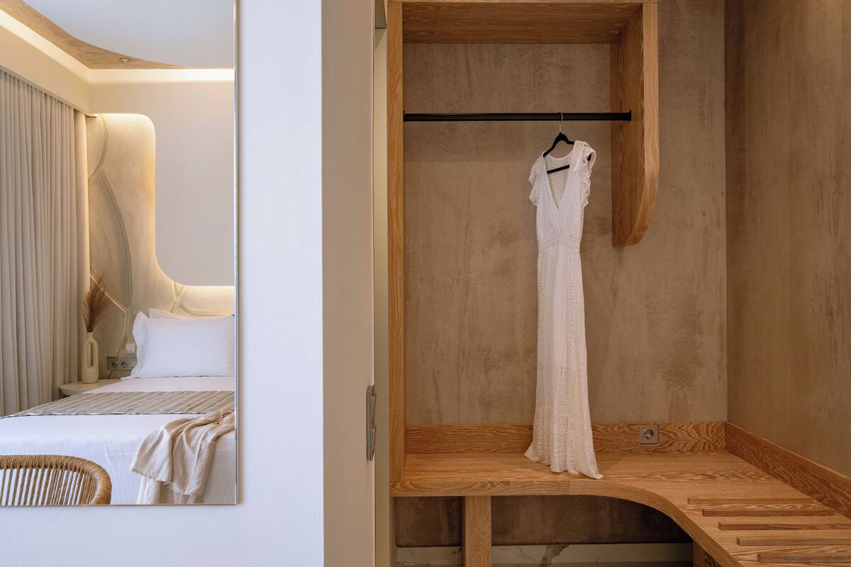 A bedroom with a bed, a wooden bench, and a hanging dress.