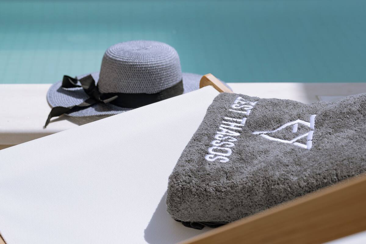 A beachside view with a lounge chair, a hat, and a towel with a logo.