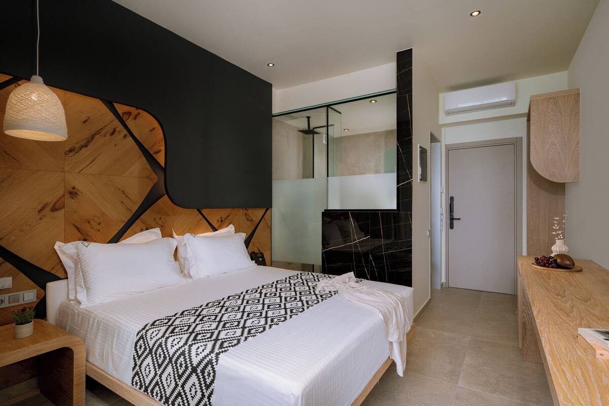 A modern bedroom with a large bed, a wooden headboard, a bedside table, and a hanging light fixture.
