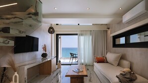 Una sala de estar moderna con piso de mármol, televisor de pantalla plana, mesa de centro de madera, sofá y vista al mar.