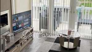 A living room with a TV, a sofa, a coffee table, and a balcony with a view. - Luxury Caravan in Towyn North Wales (Abergele)