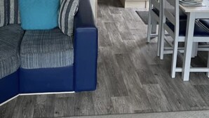 A modern living room with a blue sofa, a dining table with chairs, and a patterned rug. - Luxury Caravan in Towyn North Wales (Abergele)