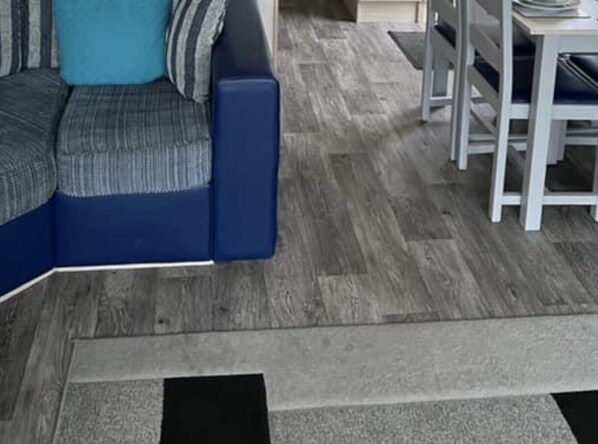 A modern living room with a blue sofa, a dining table with chairs, and a patterned rug. - Luxury Caravan in Towyn North Wales (Abergele)