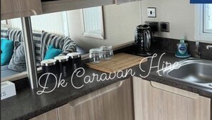 A compact kitchenette with wooden cabinets, a microwave, a coffee maker, and a sink. - Luxury Caravan in Towyn North Wales (Abergele)