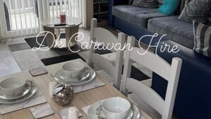 A dining area with a wooden table set for four, surrounded by white chairs. - Luxury Caravan in Towyn North Wales (Abergele)