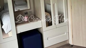 A bedroom with a bunk bed, a wardrobe with a mirror, and a small blue storage box. - Luxury Caravan in Towyn North Wales (Abergele)