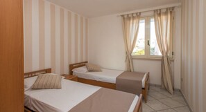Une chambre avec deux lits simples, une fenêtre avec des rideaux et un mur à rayures.