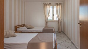 A room with two single beds, a window with curtains, and a door.