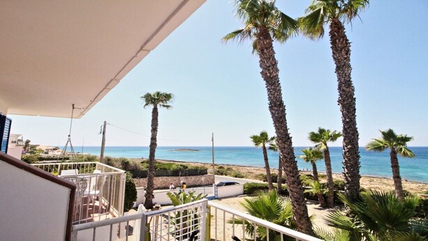 A balcony with a view of the beach, palm trees, and the sea.