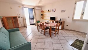 A compact living space with a dining area, a sofa, a TV, and a small kitchen area.