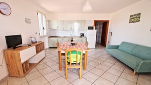 A compact living space with a dining table, a sofa, a TV, and a kitchen area.