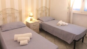 Een hotelkamer met twee eenpersoonsbedden, een nachtkastje met een lamp, een raam met gordijnen en een hanglamp.