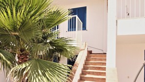 Een trap die leidt naar een balkon met een palmboom en een gebouw met een geometrisch gevelontwerp.